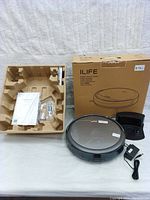 Robotic vacuum cleaner with original packaging, charger, power adapter, user manuals, and accessories arranged on a table.