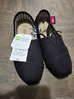 Top view of new black women's shoes with tags showing Better Cotton Initiative label and size 6 sticker