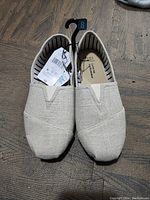 Front view of the beige fabric slip-on shoes showing toe details and size 8 hanger.