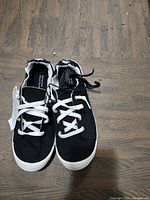 Front view of pair of black women's shoes on wooden surface, showing white laces and soles.
