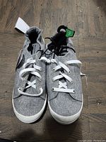 Photo of front view of gray women's shoes size 9 on wooden floor showing fabric texture, white laces, and white rubber soles.