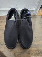 Top view of new men's black slip-on shoes size 11 with tags and size label attached.