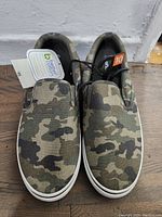 Front view of the men's camouflage slip-on shoes showing the size 10 tag and attached product tag.