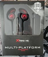 Front view of the earbuds in original packaging showing black and red earbuds with gaming themed design and branding.