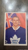 Front side of the card displaying a color portrait of Carl Brewer in a Toronto Maple Leafs jersey with a red and blue background including a flag motif.