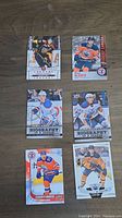 Front view of 6 Connor McDavid hockey cards arranged on a wooden surface showing various sports card designs and player images in Edmonton Oilers uniform.