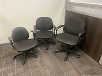 Three black office chairs with fabric upholstery and armrests on wheeled bases. Slightly different sizes, untested condition.