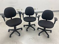 Photo showing three black office chairs with fabric seats and backs, adjustable armrests, five-legged caster bases.