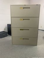 Front view of beige metal 4 drawer lateral filing cabinet with recessed handles and brass label holders.