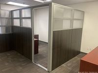 Photo showing modular office wall panels in woodgrain finish with frosted glass upper sections and aluminum frames creating a cubicle space in office.