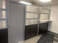Front view of modular office wall including door panel, translucent window panels above dark wood lower sections, and metal framing.