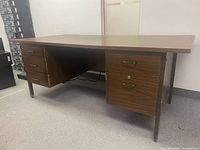 Front-left side angle of the brown wooden office desk showing drawers on both sides and four legs.