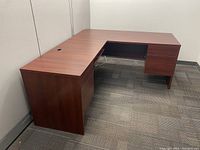 L shaped desk with dark wood finish viewed from front and side showing drawers and keyboard tray.