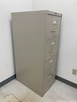 Side angled view of the vertical filing cabinet showing four metal drawers with handles and label holders, condition visible with minor wear and dirt marks.