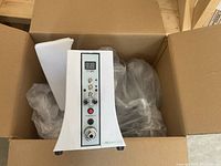 White Bella vacuum therapy machine with control panel and power switch, shown inside packing box with protective wrapping.