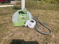 Bissell Little Green portable carpet cleaner and hose nozzle sitting on grass outdoors.