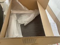 Box showing flat packed cabinet panels with dark wood grain finish and foam wrapping inside.