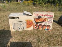 Two boxed kitchen appliances outdoors: Philips fryer on left, Dazey Pick-A-Pocket snack maker on right.