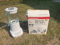 Photo showing the assembled white Hamilton Beach blender with glass jar and original juicer box placed on grass.