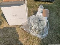 Photo showing the hanging light fixture with glass pieces inside a metal frame and the open box on grass.