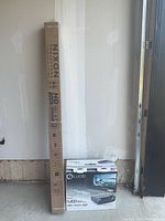 Nixon Self Lock Screen in long cardboard box and Lucid LED projector box side by side on concrete floor.