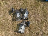 Three black outdoor hexagonal wall lantern lights on grass surface, bulbs included, some rust and dust visible