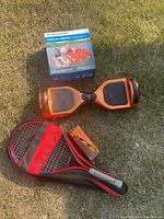 Photo shows orange hoverboard, black and red badminton racket with shuttlecock and small shuttlecock pack.
