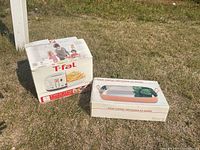 Photo showing T-fal Filtra One fryer box next to a solid copper rectangular pan box on grass.