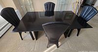Black rectangular dining table with four matching uniquely designed black chairs shown from an angled perspective.