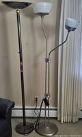 Photo of two floor lamps side by side; black taller lamp and silver shorter lamp with two white lampshades