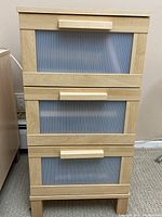 Front view of small IKEA Ameboma 3-drawer chest showing beech wood frame and ribbed plastic drawer fronts with wooden handles.