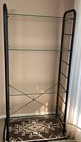 Full view of black metal frame shelving unit with four glass shelves, showing overall size and design.