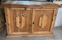 Front view of the vintage Mexican wooden cabinet showing two paneled doors with decorative raised middle panels and black metal latch lock.