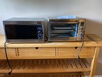 Photo of the Panasonic microwave and Hamilton Beach toaster oven side by side on a wooden shelf.
