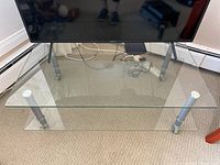 Glass and metal TV stand front view showing transparent glass top shelf and metal legs with castors.