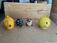 Four piggy banks lined up on cardboard: yellow dog, black pig, beaver with flag, yellow smiley face