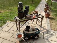 Metal folding laundry stand with wheels outdoors on paved walkway, holding plastic owl statues and various garden items around it.
