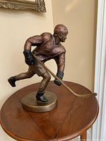 Full view of the Austin Productions hockey player sculpture showing dynamic pose and bronze and copper paint finish.