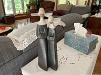 Two matte Gres finish nuns figurine on a white cloth with a couch in the background.