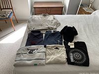 Full view of all items including sweaters, shirts and a hat laid out on a bed