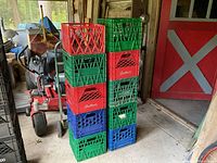 View of 10 stacking milk crates in red, blue, and green colors with visible brand names Sealtest and Avis, stacked near a door inside a garage