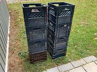 Two stacks of plastic milk crates, mostly dark blue/black with one brown crate visible at base, outdoors on grass near a building.