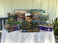 Photo showing 10 boxed puzzles arranged on a table, featuring the titles Mona Lisa by Clementoni, Ron Bayens 550 piece, Nights & Day 1000 piece, and others.