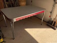 View showing the full kitchen table with grey marble-patterned top, red scalloped trim beneath, and chrome tubular legs in a lighted room.