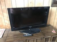 Full view of the Samsung 31 inch LCD TV on a black stand with the remote control placed in front of it.