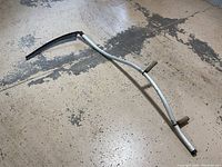 Full view of the sickle showing the curved aluminum handle with two wooden hand holds and the curved blade covered by a black sheath.