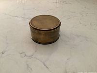 Closed brass pocket sextant, cylindrical drum shape, top surface plain.