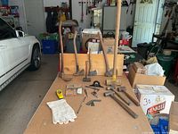 Overview of all tools arranged on a wooden surface including axes, hammers, sledgehammer, gloves, and measuring tape