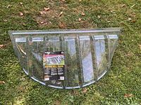 Full view of the clear curved heavy duty window well cover placed on grass.