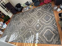 Full view of large gray area rug laid flat on hardwood floor with geometric trellis pattern in beige.